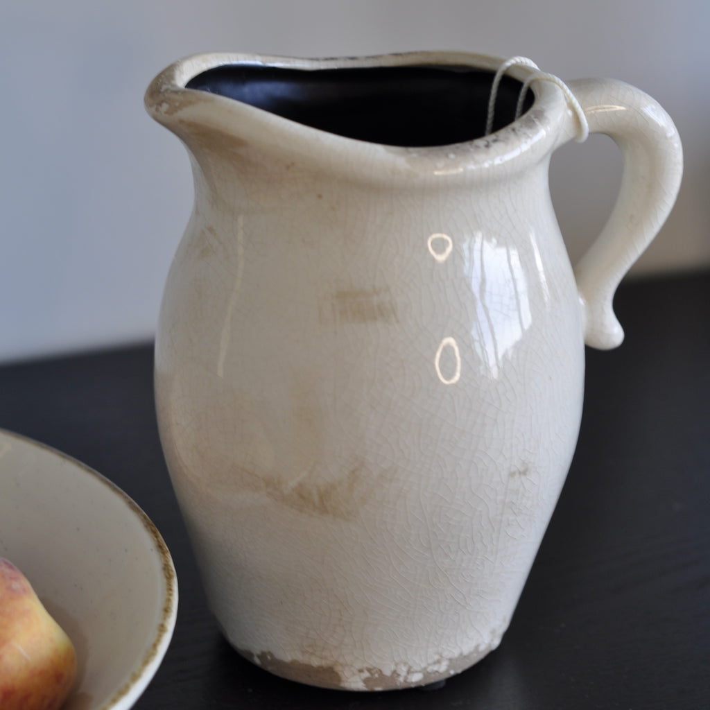 Antique ceramic pitcher with a glossy glaze, cream and beige color palette, and subtle floral pattern.