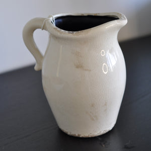 Antique ceramic pitcher with a glossy glaze in cream and beige colors, featuring a subtle floral pattern and a smooth glazed crackle surface.