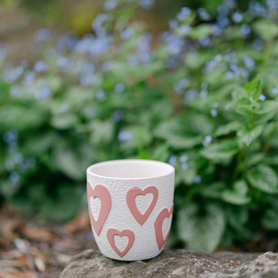 Ceramic cup with heart patterns on a rock with greenery in the background