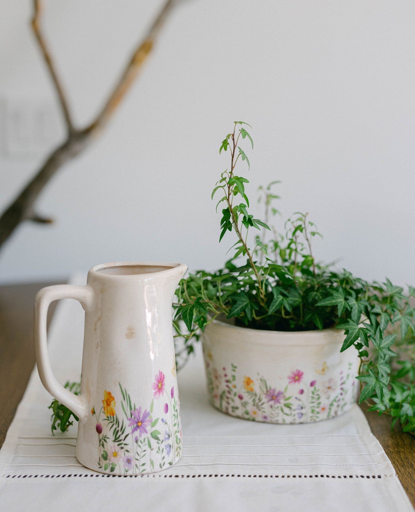 Decorative ceramic pitcher and plant pot with floral designs on a white surface.