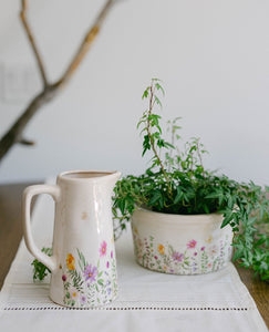 Decorative ceramic pitcher and plant pot with floral designs on a white surface.