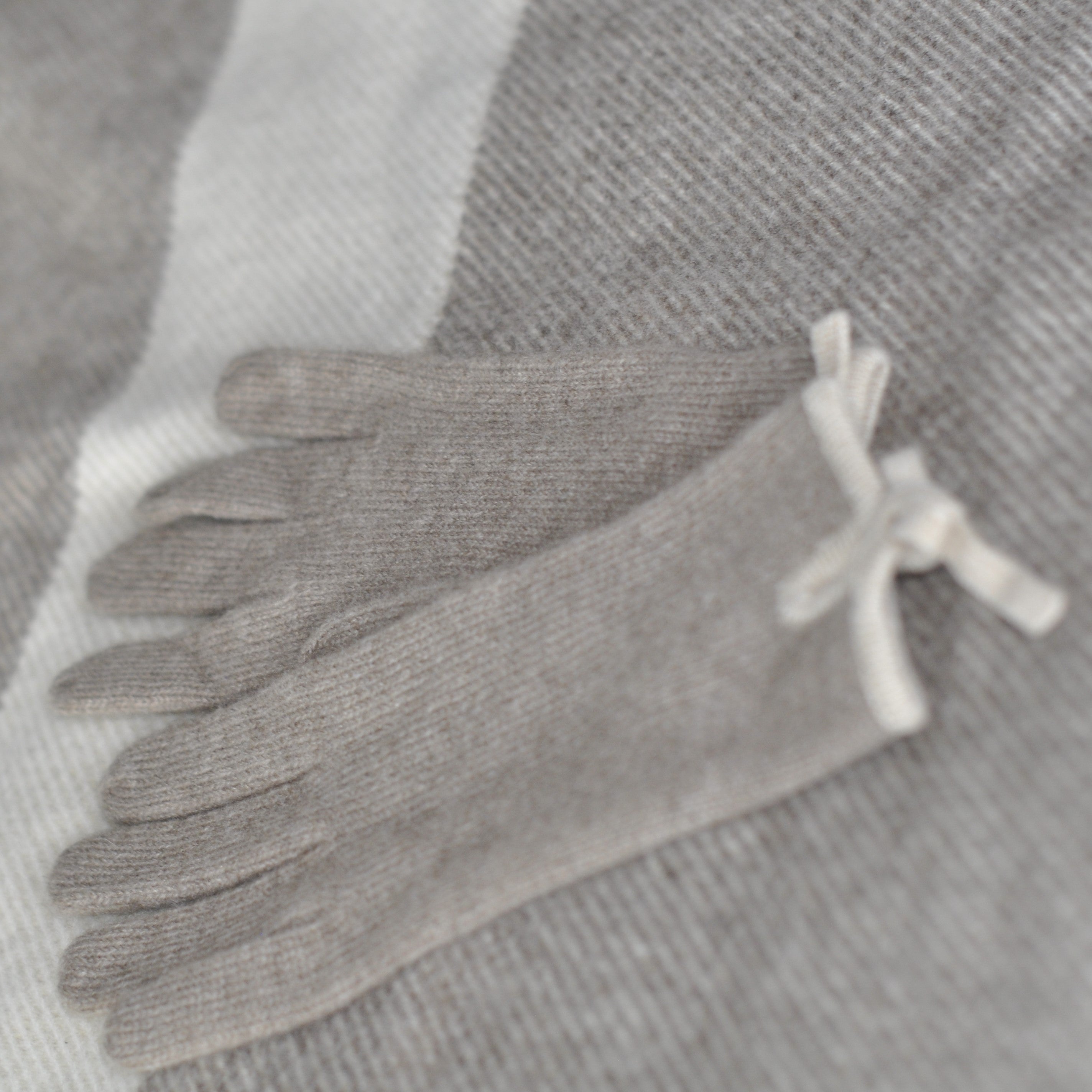 A pair of cream-colored cashmere gloves laid out flat on a grey background, showing the texture and color of the gloves.