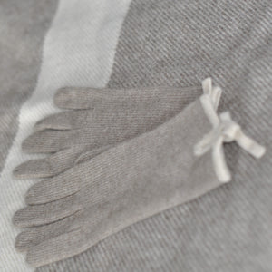 A pair of cream-colored cashmere gloves laid out flat on a grey background, showing the texture and color of the gloves.