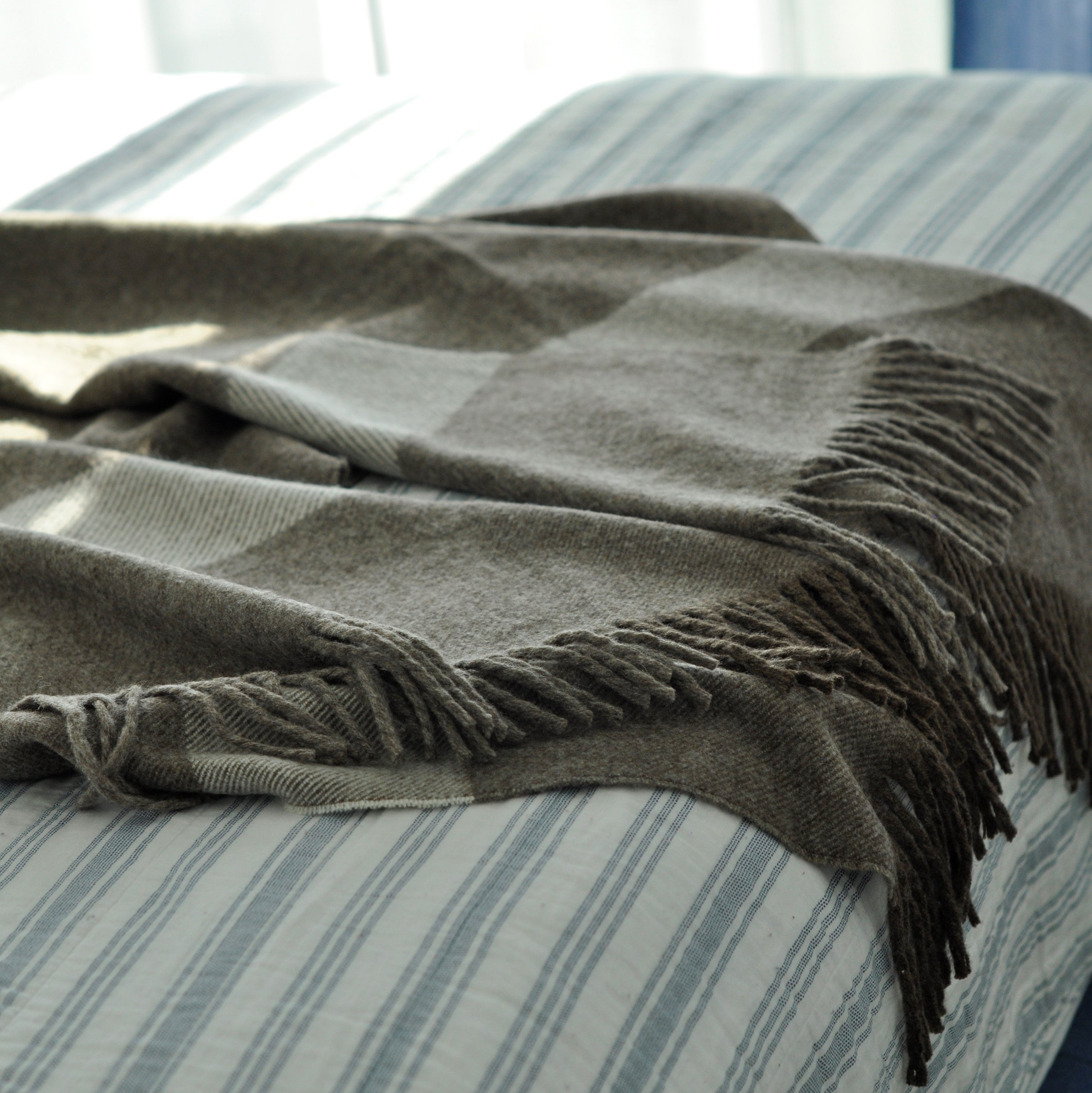 Gray blanket with fringes on a striped bed