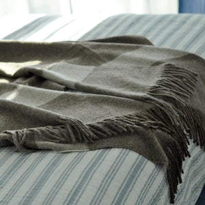 Gray blanket with fringes on a striped bed