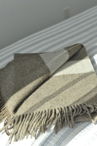 Gray and beige plaid blanket draped over a white surface with a neutral background