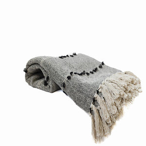 A gray cotton throw blanket with fringes, featuring embroidered designs, draped on a white background.