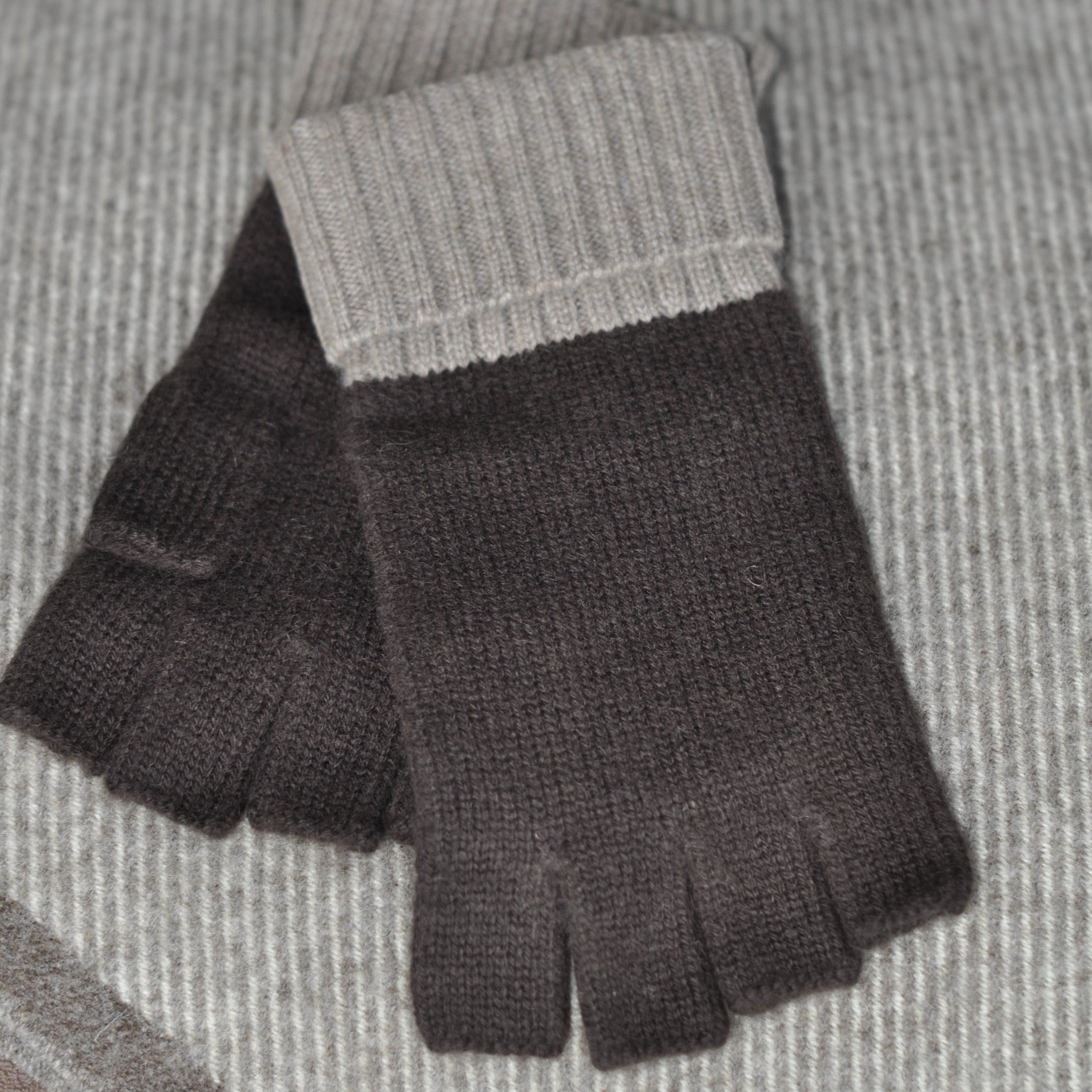 A person wearing a beige and brown cashmere beanie with a fur pom pom, and matching fingerless gloves.