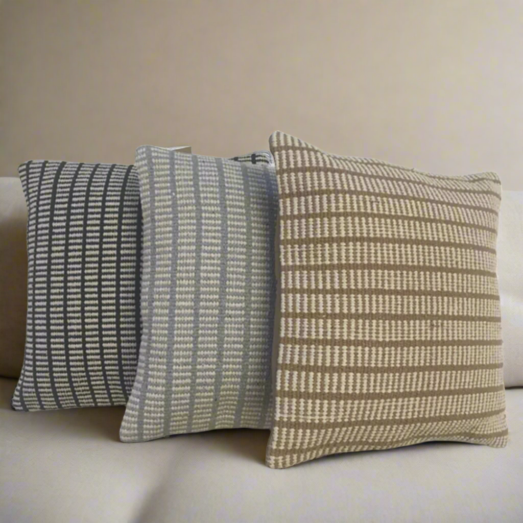 Three patterned pillows on a beige sofa against a neutral wall.