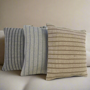 Three patterned pillows on a beige sofa against a neutral wall.