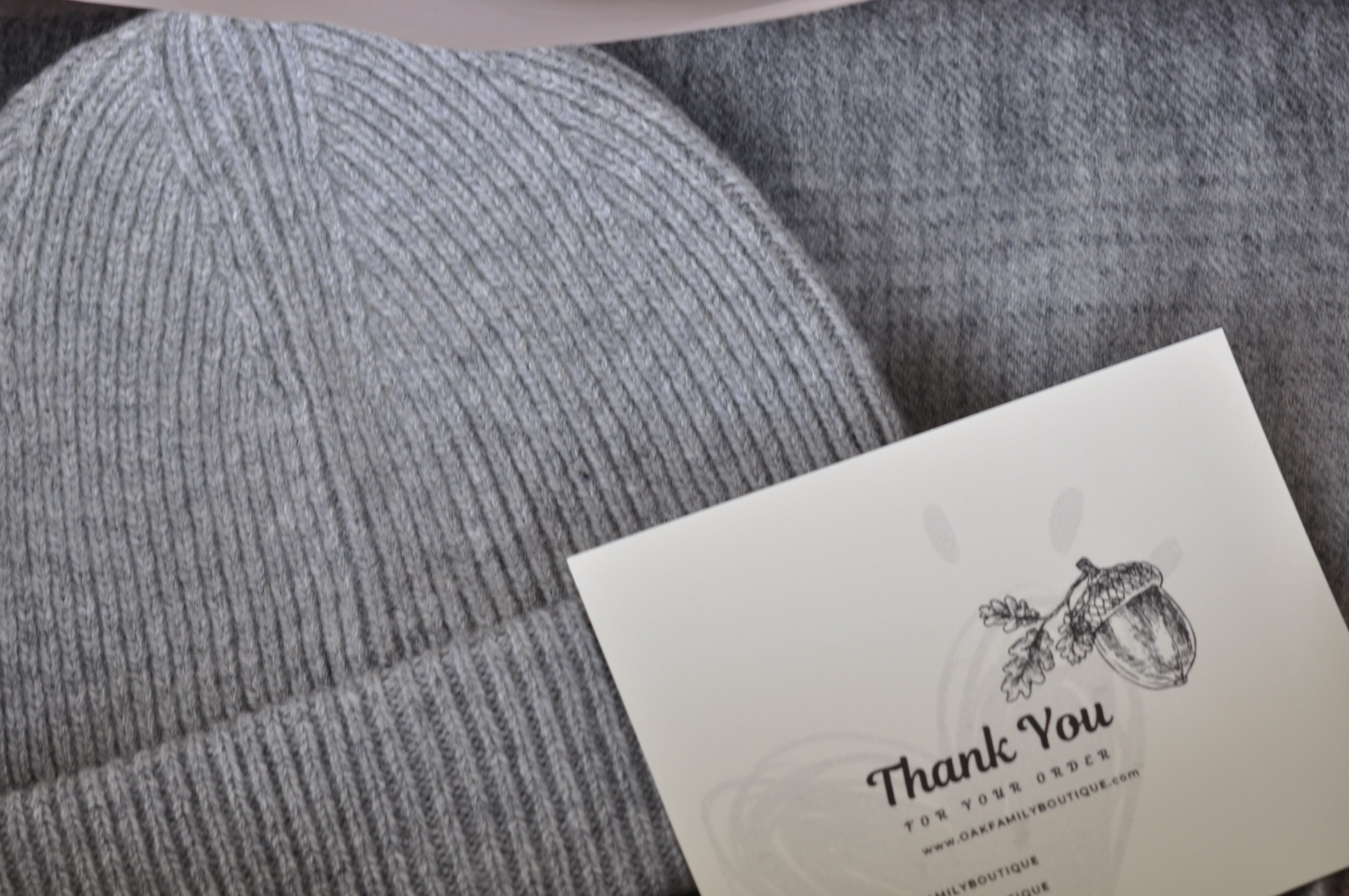 Gray knit beanie with a 'Thank You' card on a textured gray background