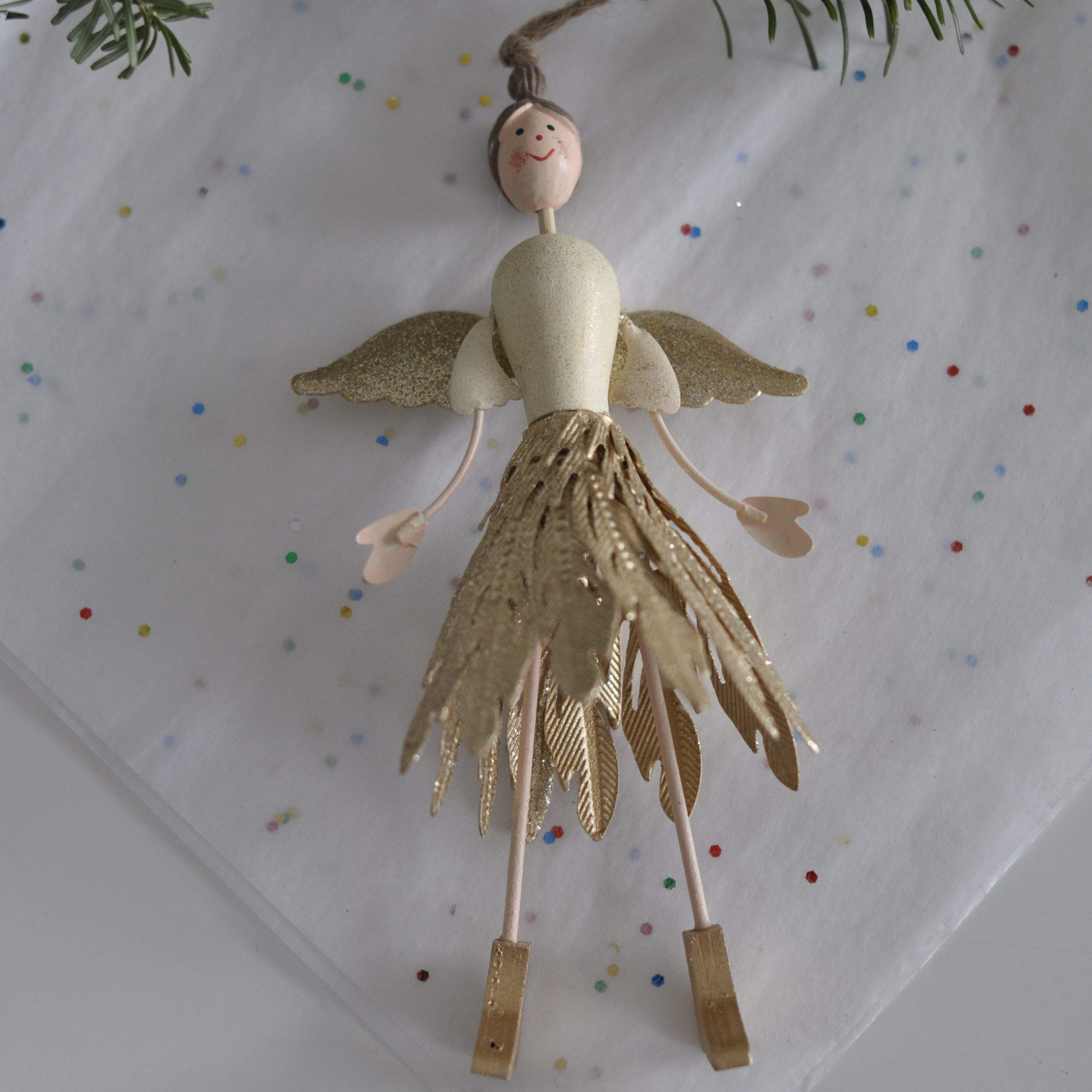 Decorative angel ornament on a white surface with colorful dots and greenery.