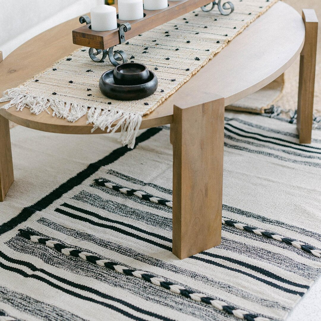 Wooden table with a decorative runner and candle holder on a striped rug.