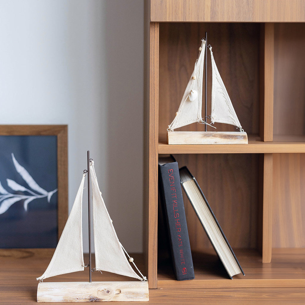 Two sailboat models on a wooden surface with books in the background.