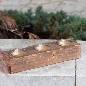 Wooden tray with three small bowls on a concrete surface with plants in the background
