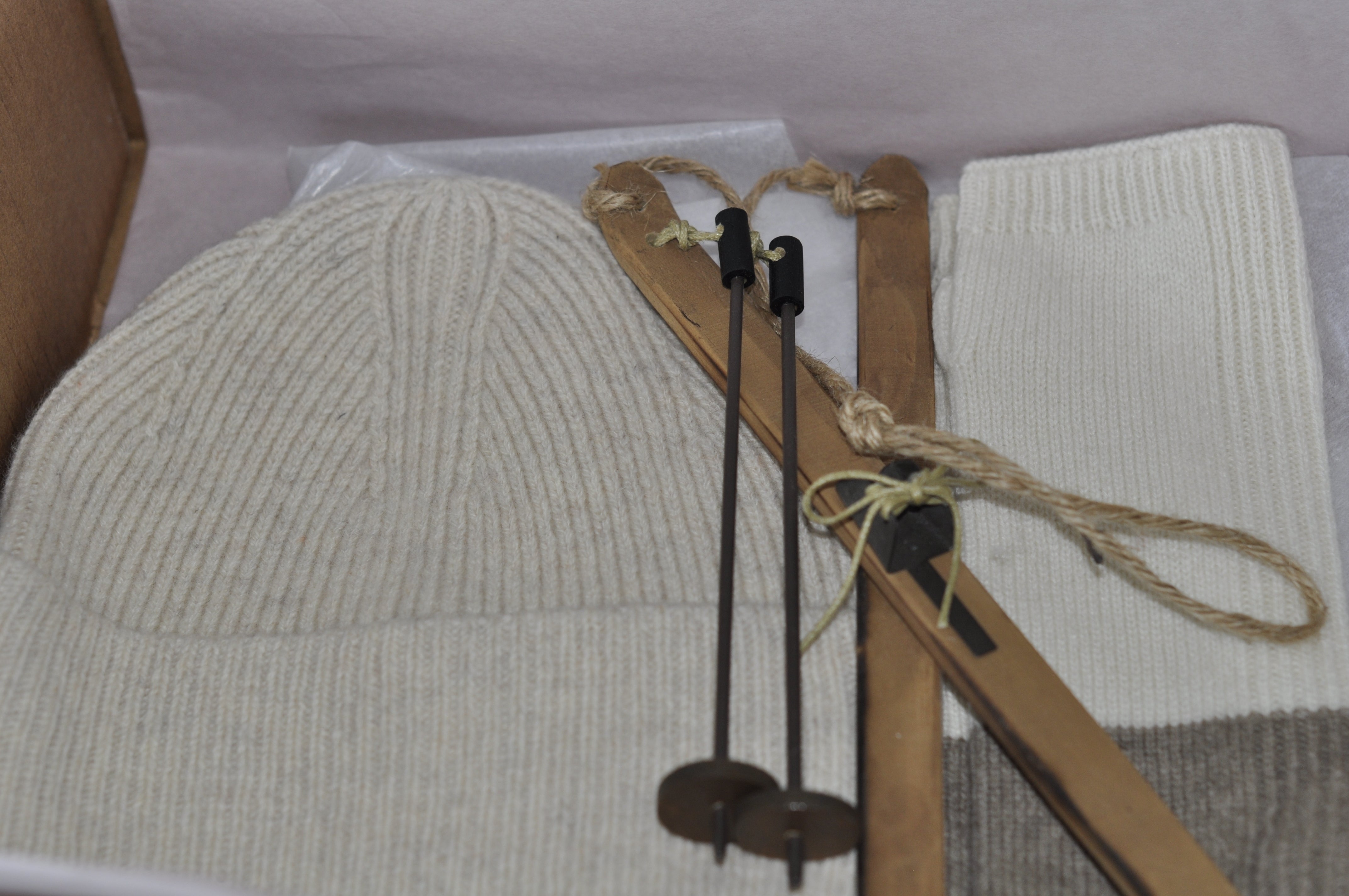 Knitted beige hat and white fabric on a wooden loom with threading tools.