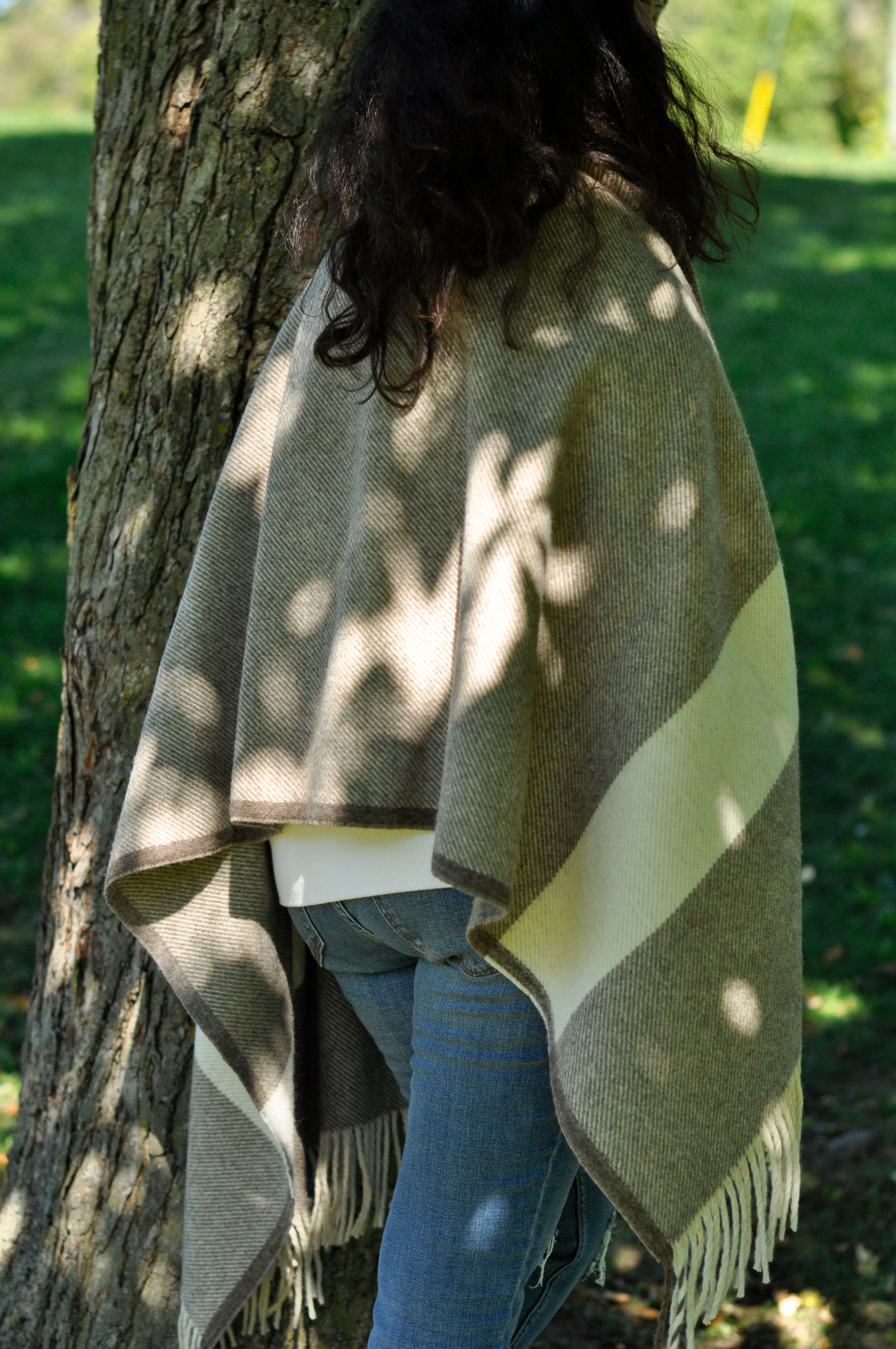 Person lying on a hammock with a green blanket and blue jeans, surrounded by trees.