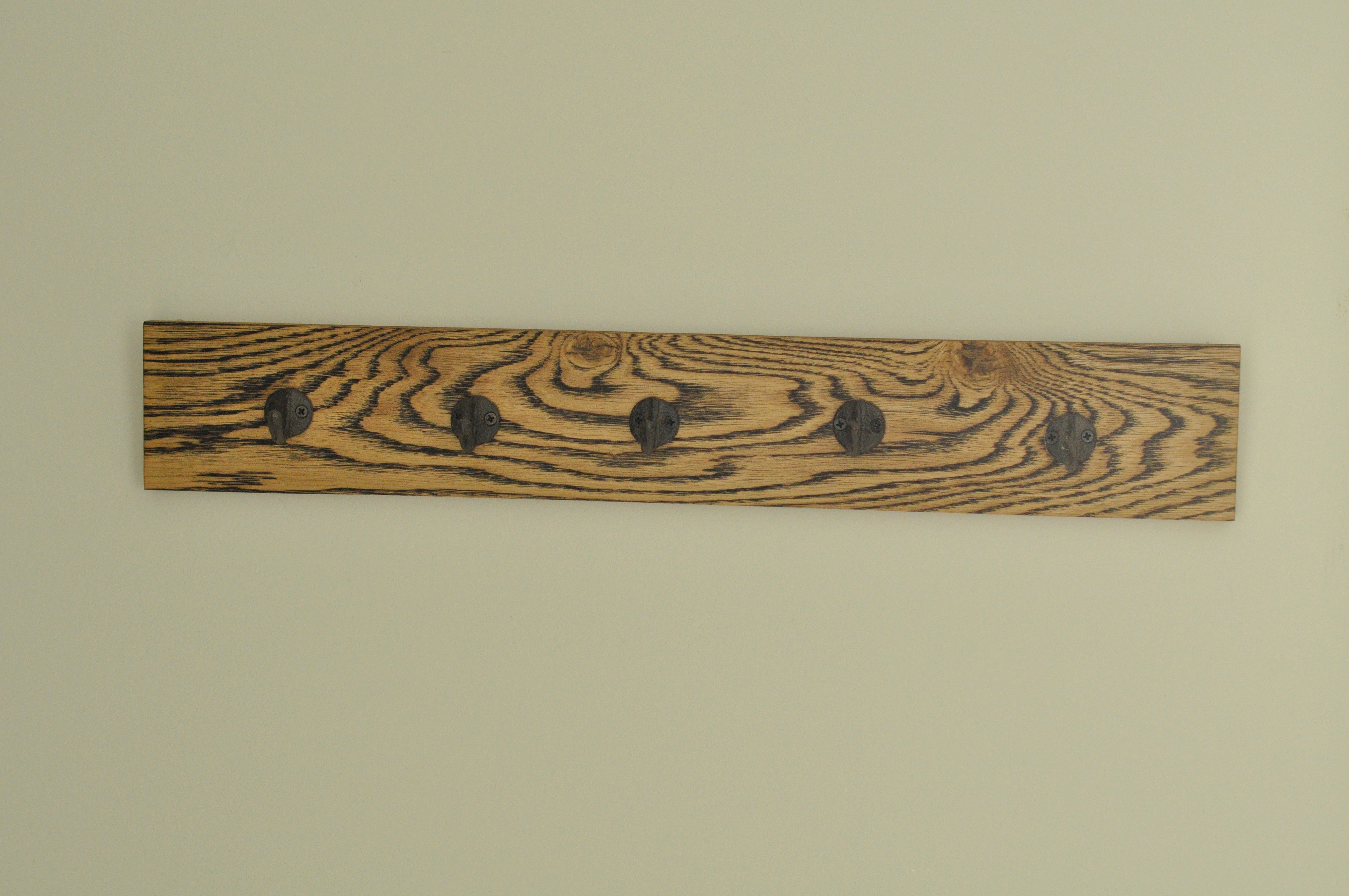This vintage-style coat rack features five brown iron hooks mounted on a wooden panel