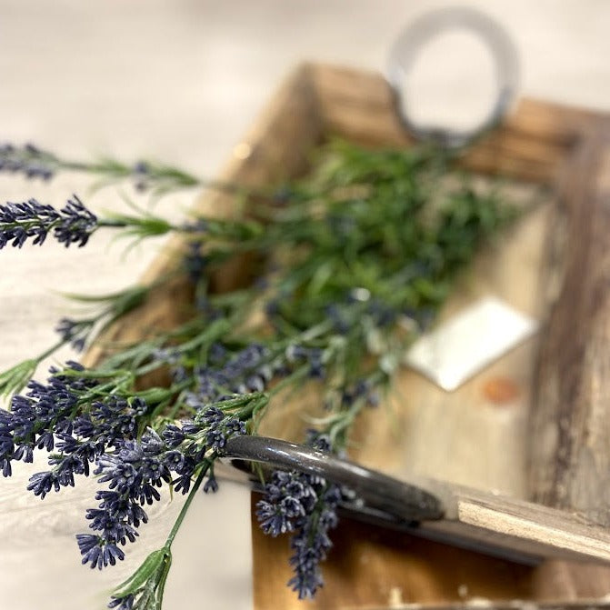 A wooden tray with metal handles, featuring a bunch of purple flowers on top.