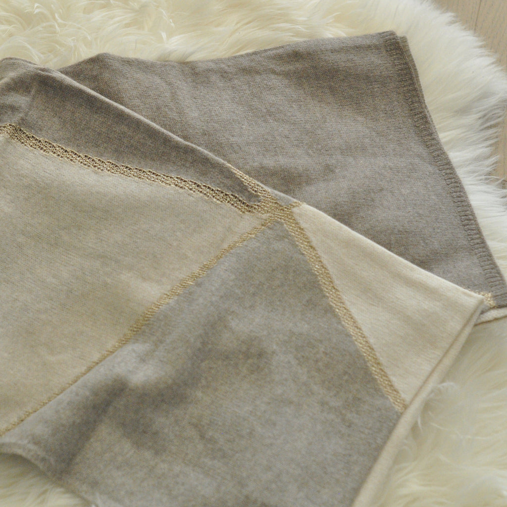 Two shades of beige cashmere shawls with a golden trim, displayed on a white furry surface.