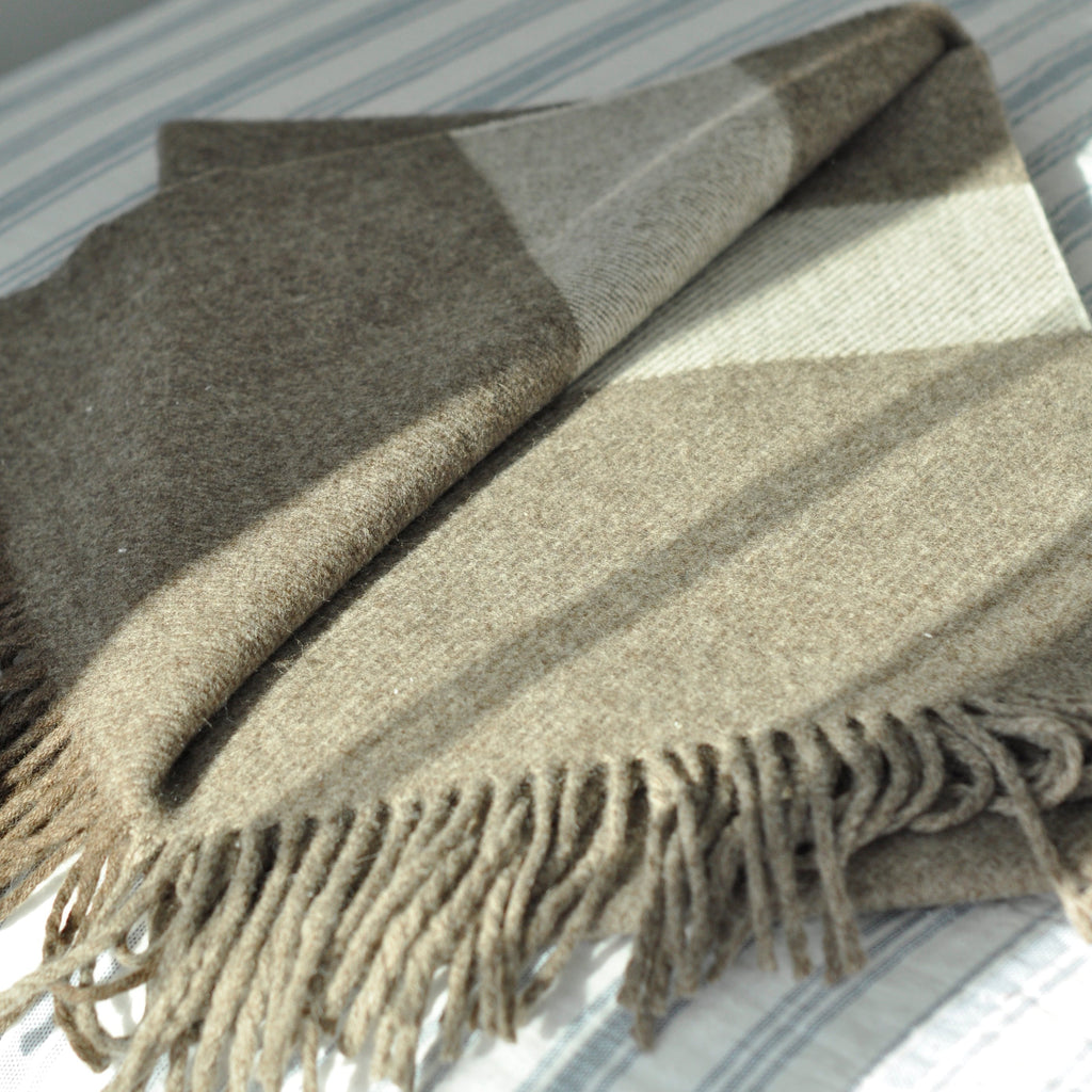 A chocolate brown wool scarf with long tassels, laid out on a bed with a striped background.
